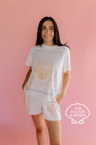 Woman wearing a white t-shirt and shorts with shell design on a pink background size L/M