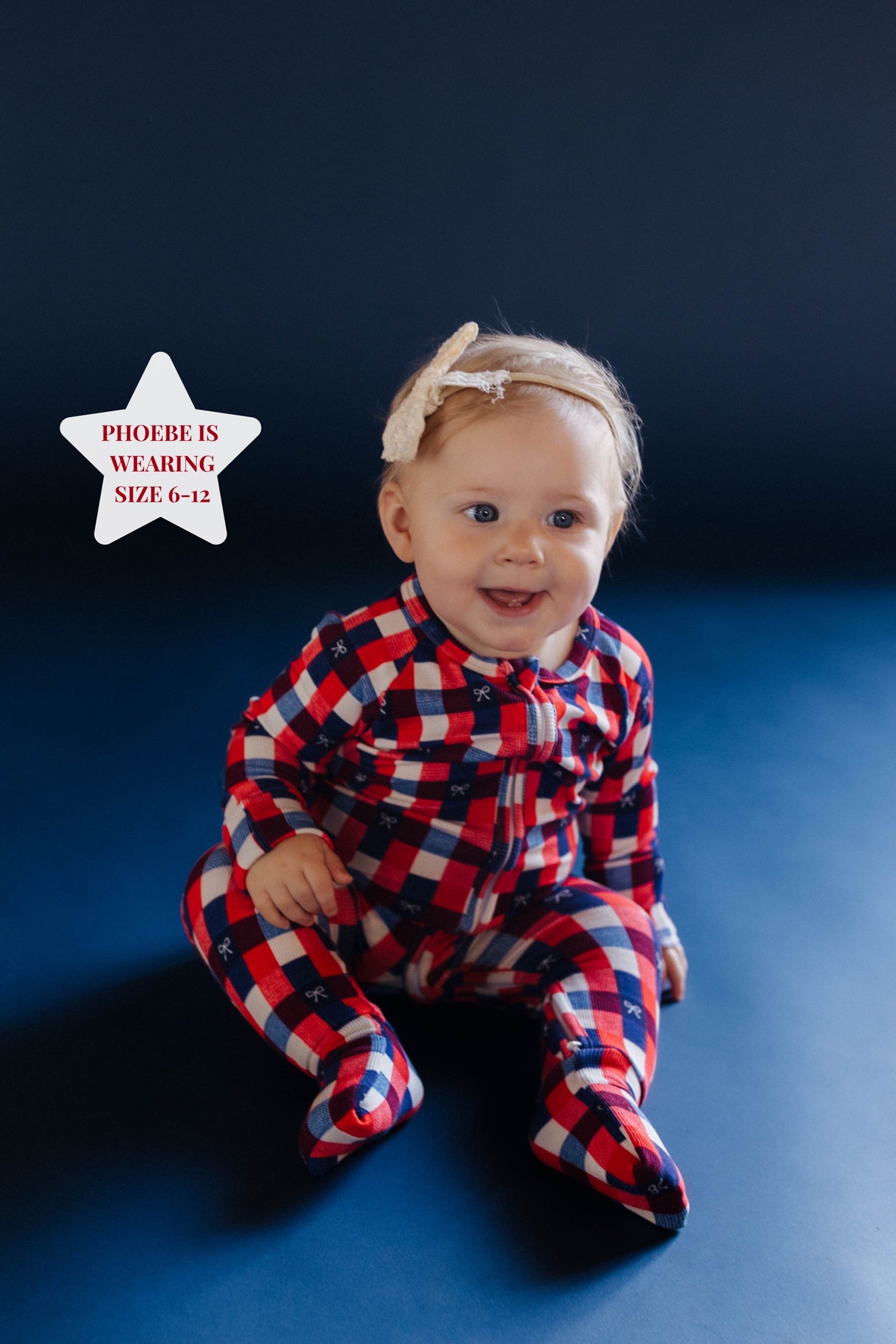 baby sitting on blue ground in red white and blue gingham onesie 