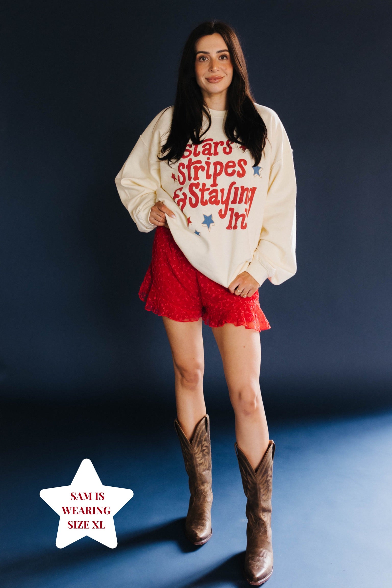 Woman wearing a graphic sweatshirt, red shorts, and brown boots on a dark background