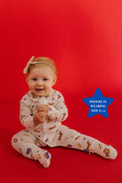 Baby sitting on a red background wearing pajamas with 4th of july icons