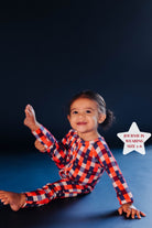 Child wearing a red, blue, and white gingham romper on a dark background