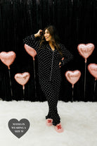 Mayra posing in front of a black wall with pink heart balloons showing the black heart pjs
