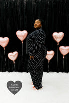 Mari wearing the size 3XL posing to the side and similing standing in front of the black wall with pink hearts 