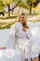 Woman wearing a striped robe sitting outdoors with trees and grass in the background