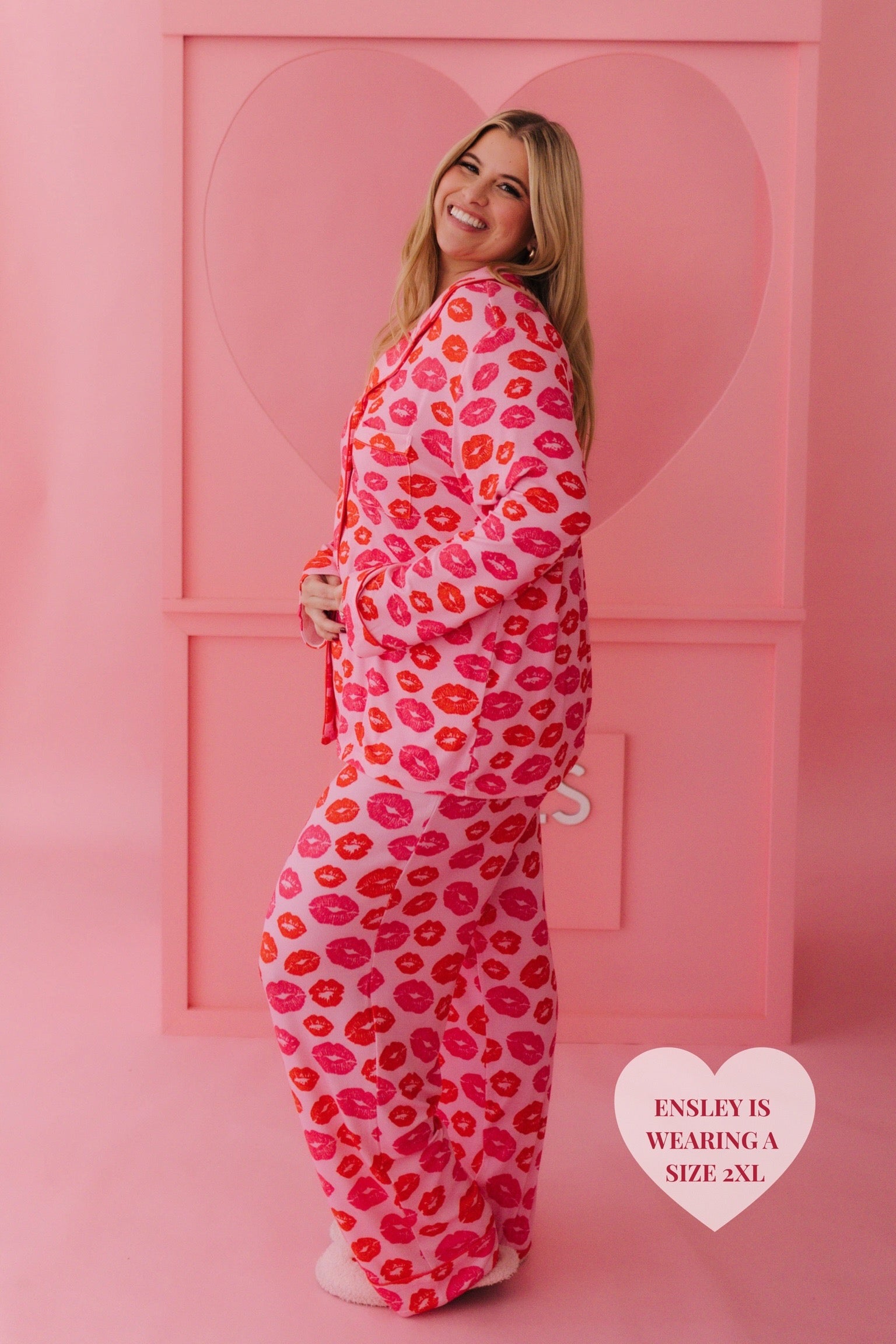Ensley smiling and posing in front of the kissing booth heart in her 2xl kiss pjs