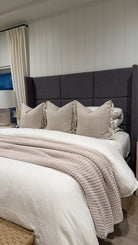 Bedroom with a bed featuring beige pillows and a textured blanket against a gray upholstered headboard.