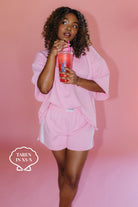 Woman in pink outfit holding a cup against a pink background