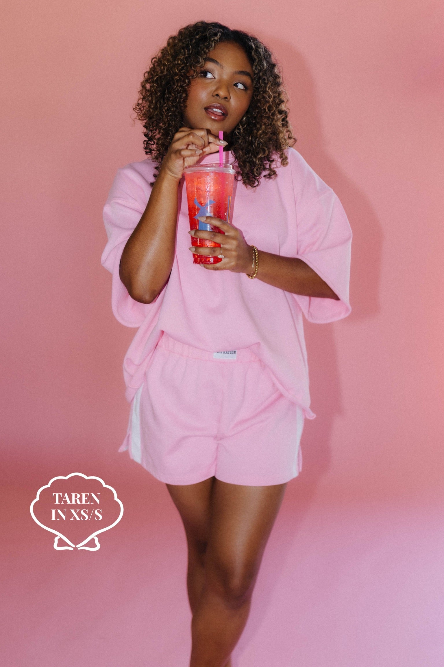 Woman in pink outfit holding a cup against a pink background