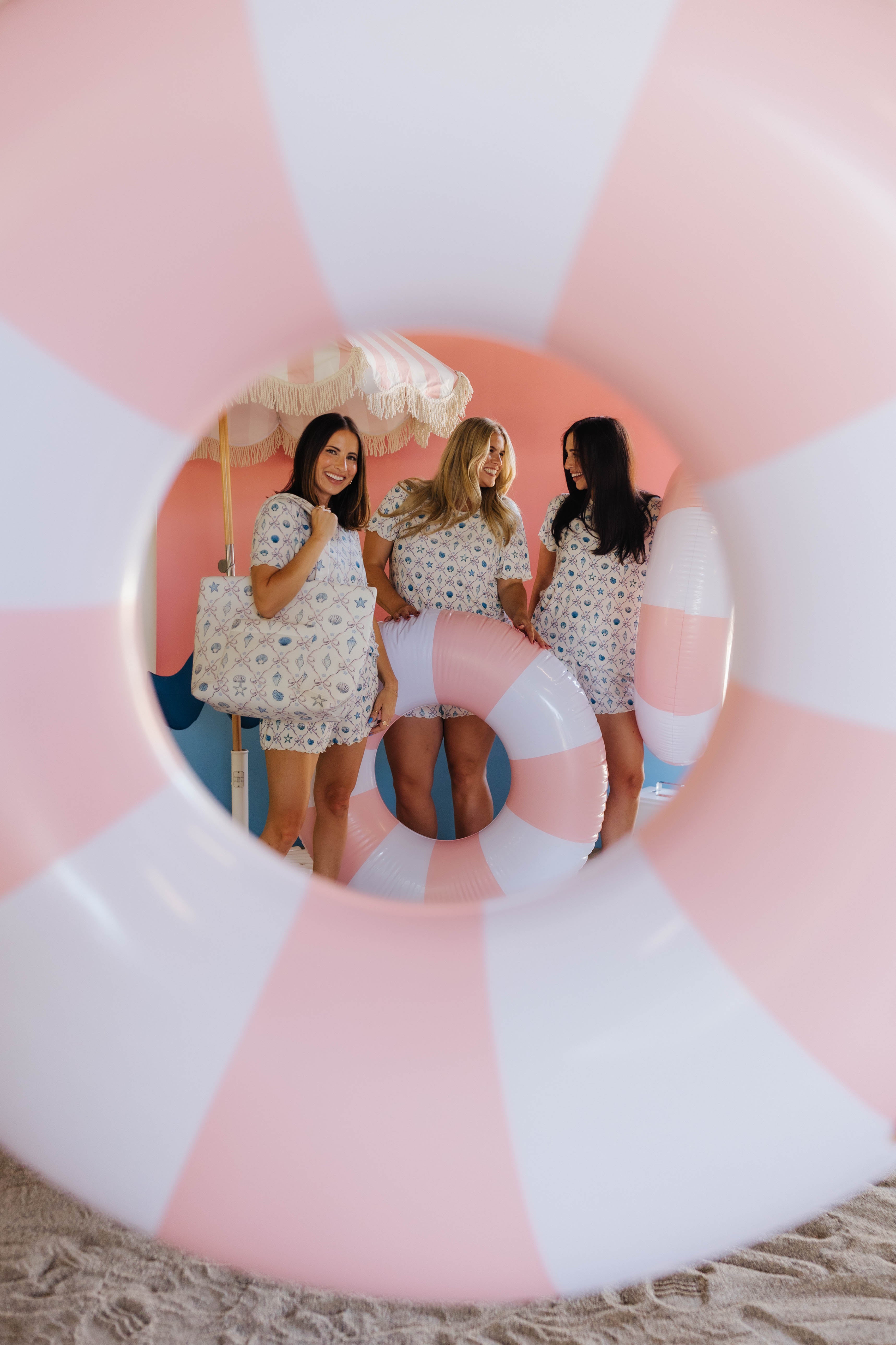 Three women in matching pjs standing behind a large pink and white inflatable ring.