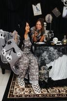 models regina and bri smiling laughing with spooky decorations in the back wearing skelly pajamas and skelly backpack/wristlet quillow 