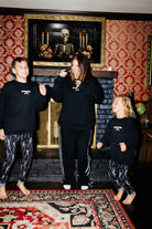 Adult and children posing by the fireplace in matching Spooky Season sweatshirts