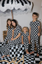 Family of four posing in black and white checkered outfits on a checkered floor with an umbrella in the background.