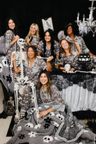 models smilin and laughing with spooky decorations wearing skeleton pajamas and wearing skeleton blanket 