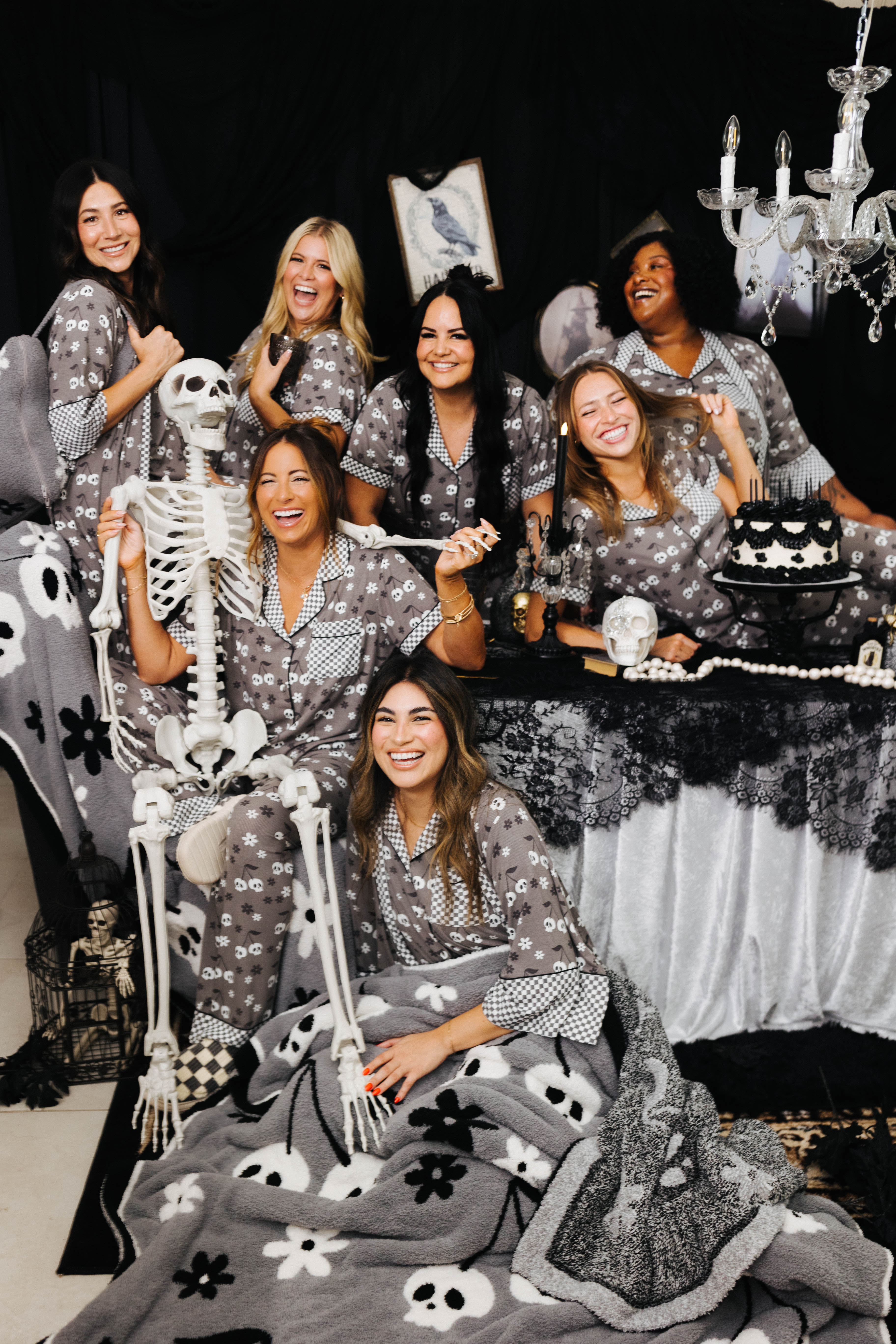 models smilin and laughing with spooky decorations wearing skeleton pajamas and wearing skeleton blanket 
