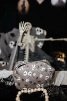 skelly cosmetic bag on table with spooky decorations in the background 
