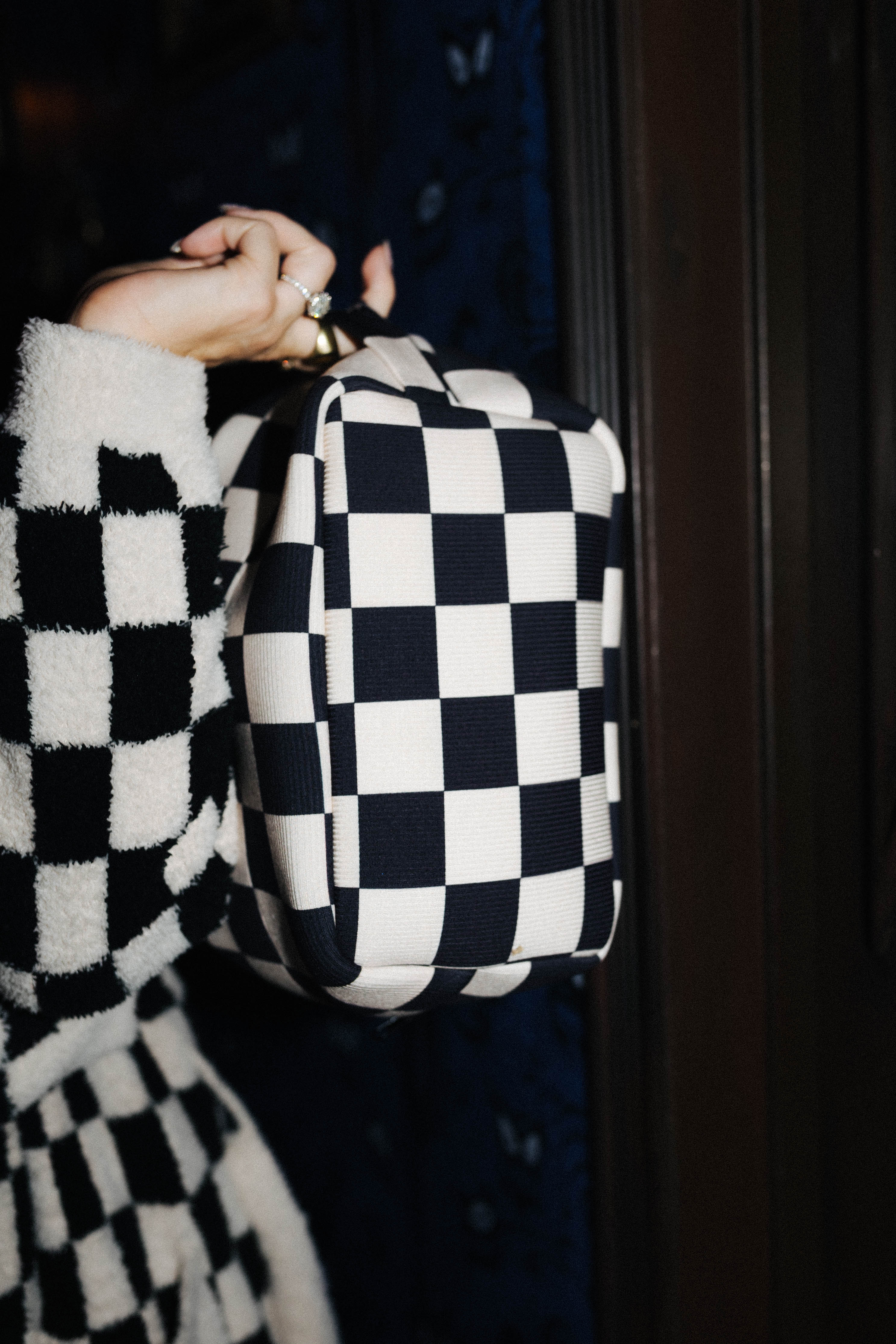 Sand and black check cosmetic bag shown from the side by its top handle