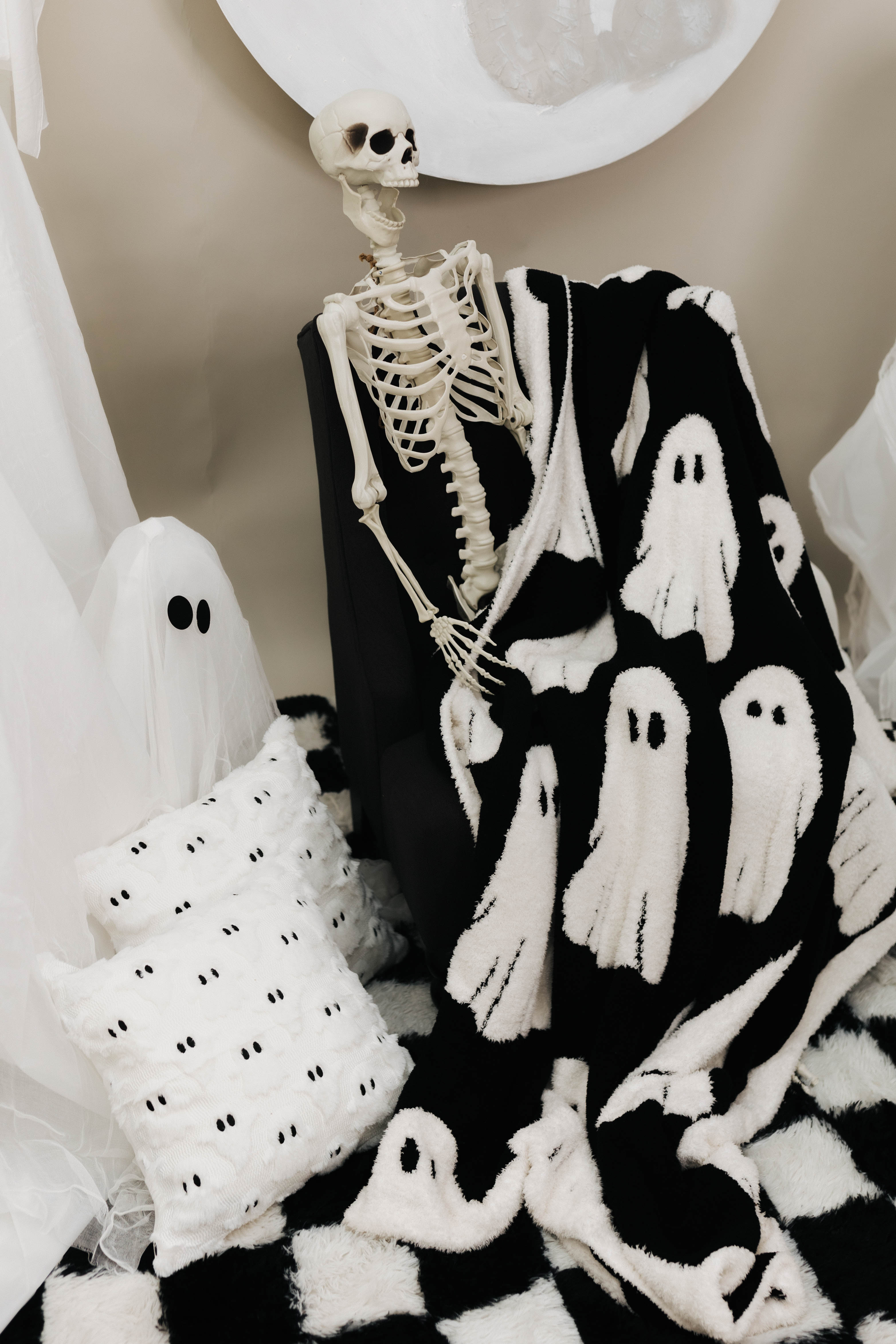 ghost blanket laying in lap of skeleton with ghost decorations in the back 