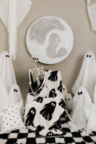 ghost blanket laying in the lap of skeleton with ghost decorations in the background 