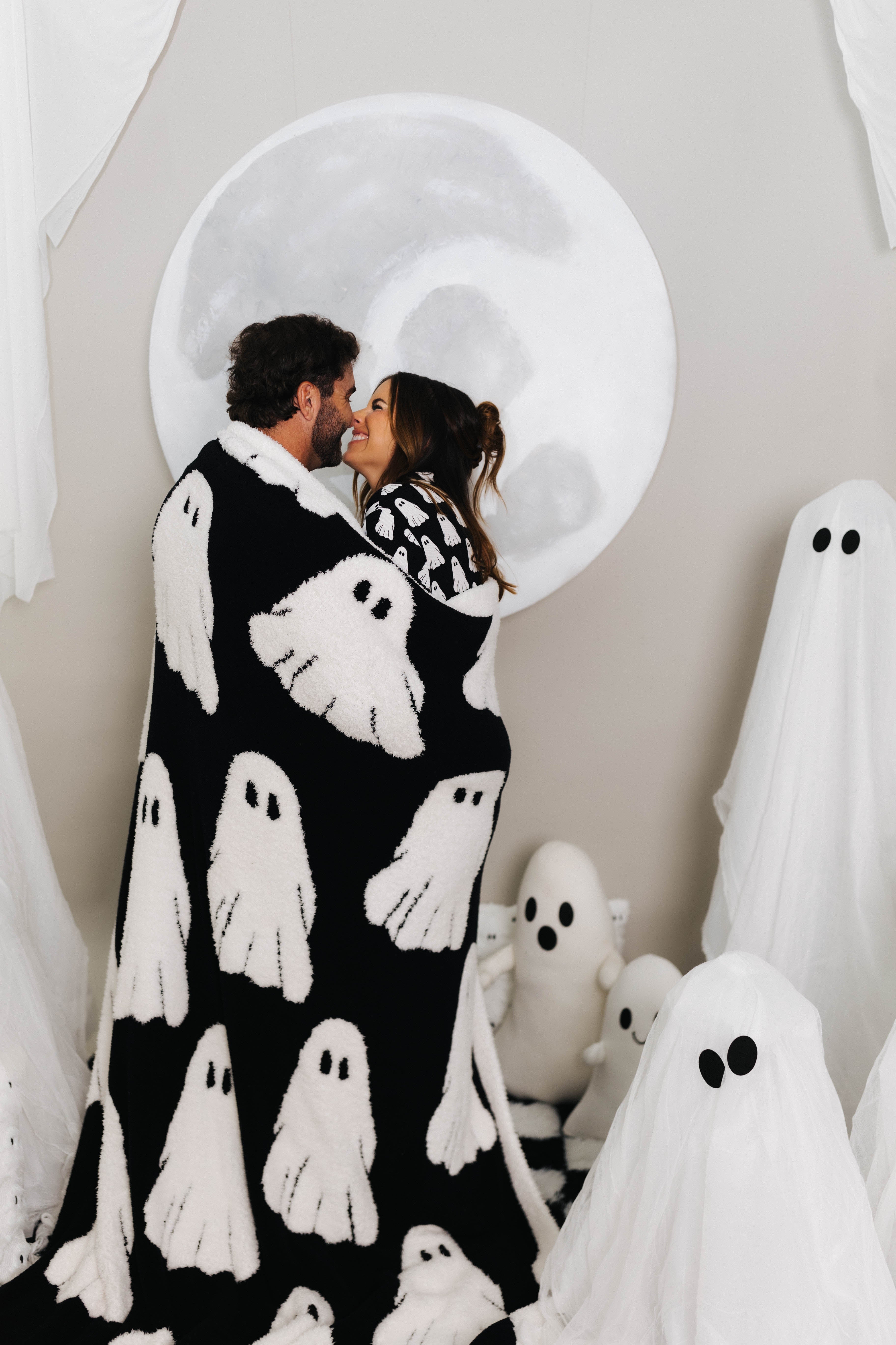 models smiling at each other with ghost blanket wrapped around them with ghost decorations in the background 