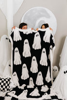 two people holding host blanket showing the black and white ghosts with ghosts decorations in the back 