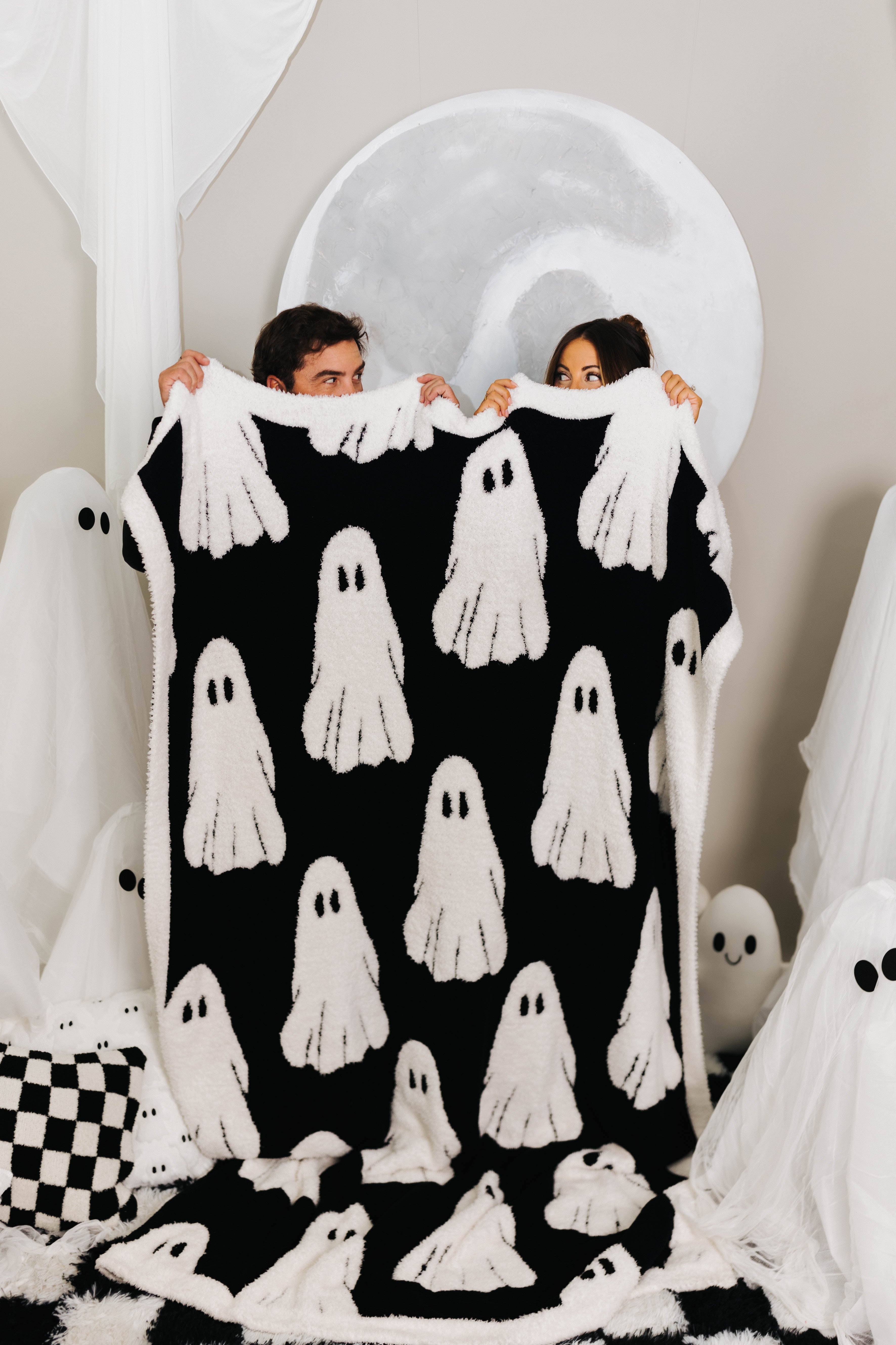 two people holding host blanket showing the black and white ghosts with ghosts decorations in the back 