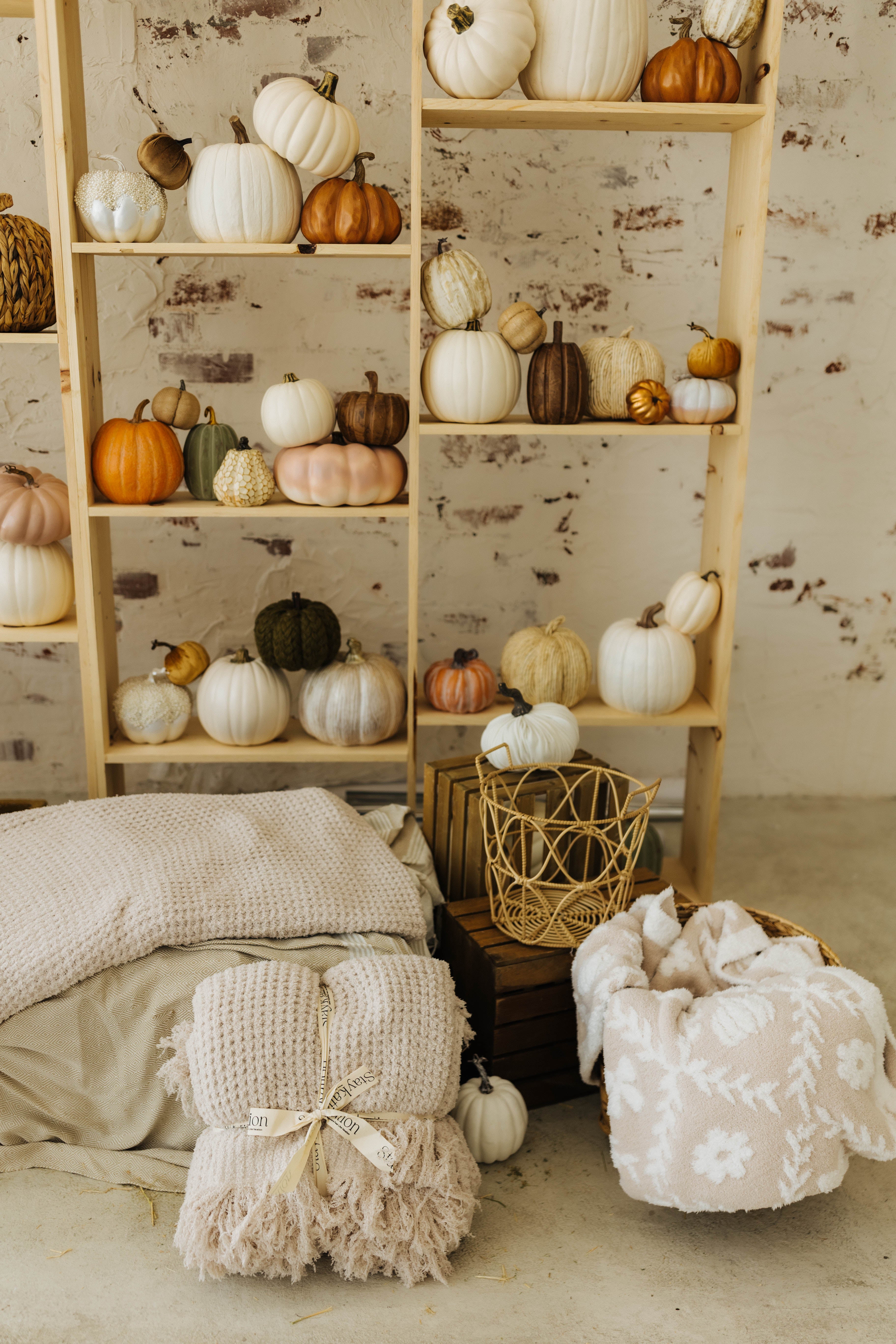 sand waffle blanket folded neatly on hay and wrapped with staykation ribbon while pumpkin blanket is neatly sitting in the basket with pumpkin decorations in the background 