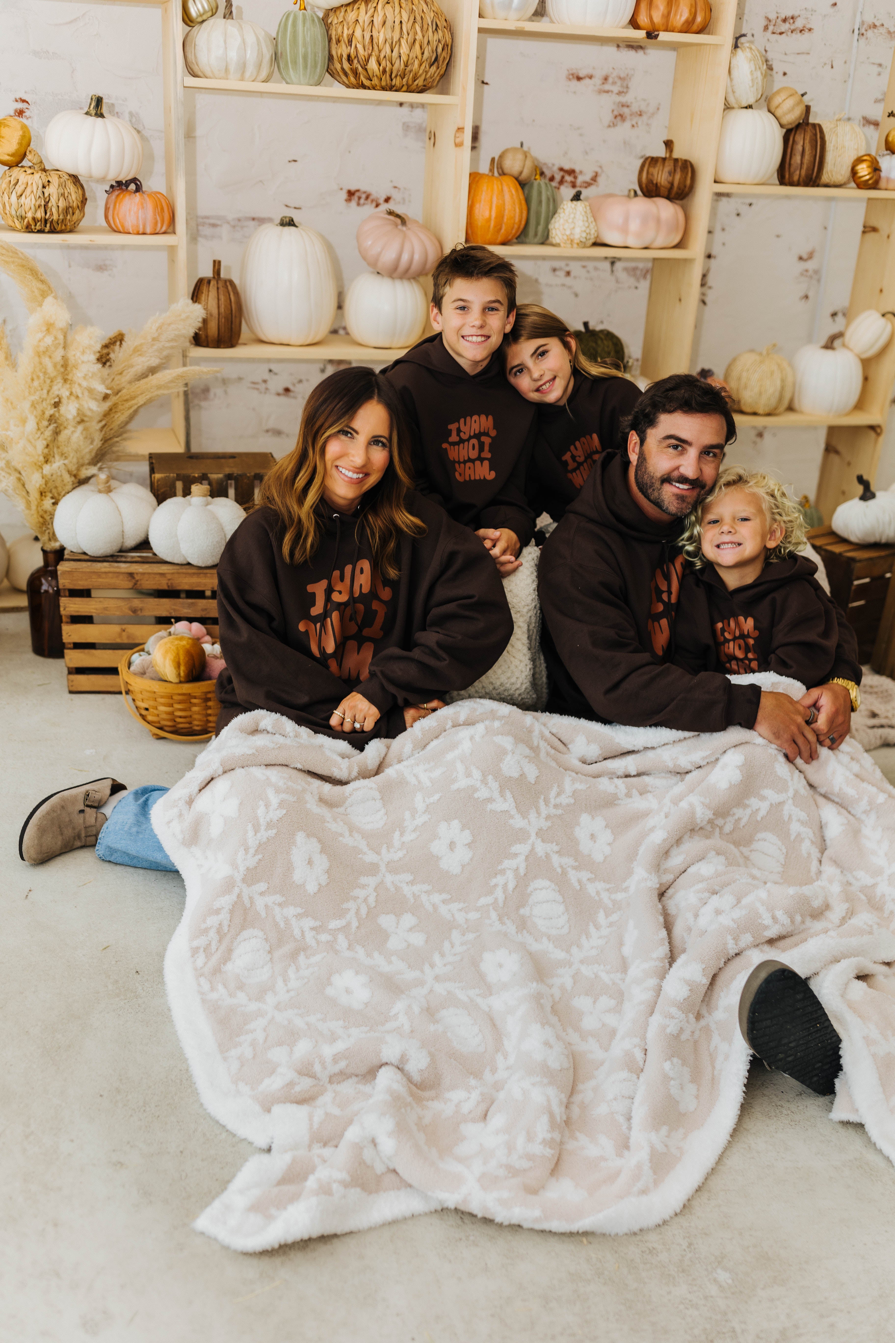 family smiling with pumpkin blanket on lap with pumpkins in the background 