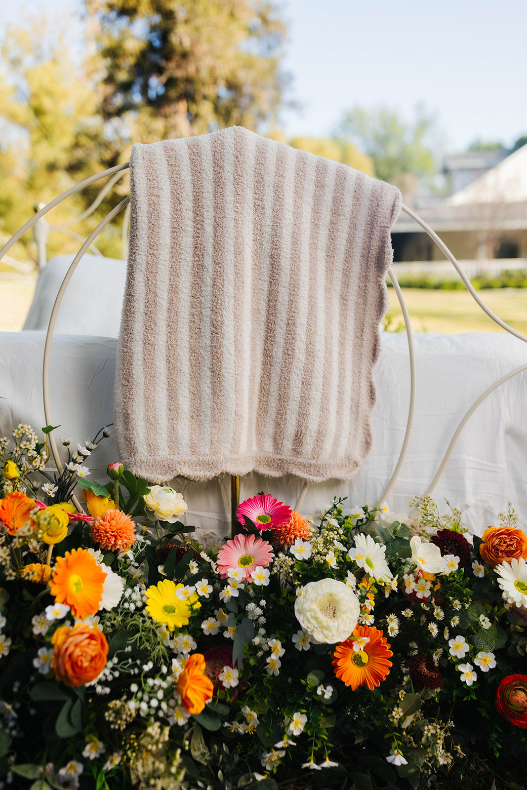 Decorative outdoor setting with a blanket draped over a bed surrounded by colorful flowers.