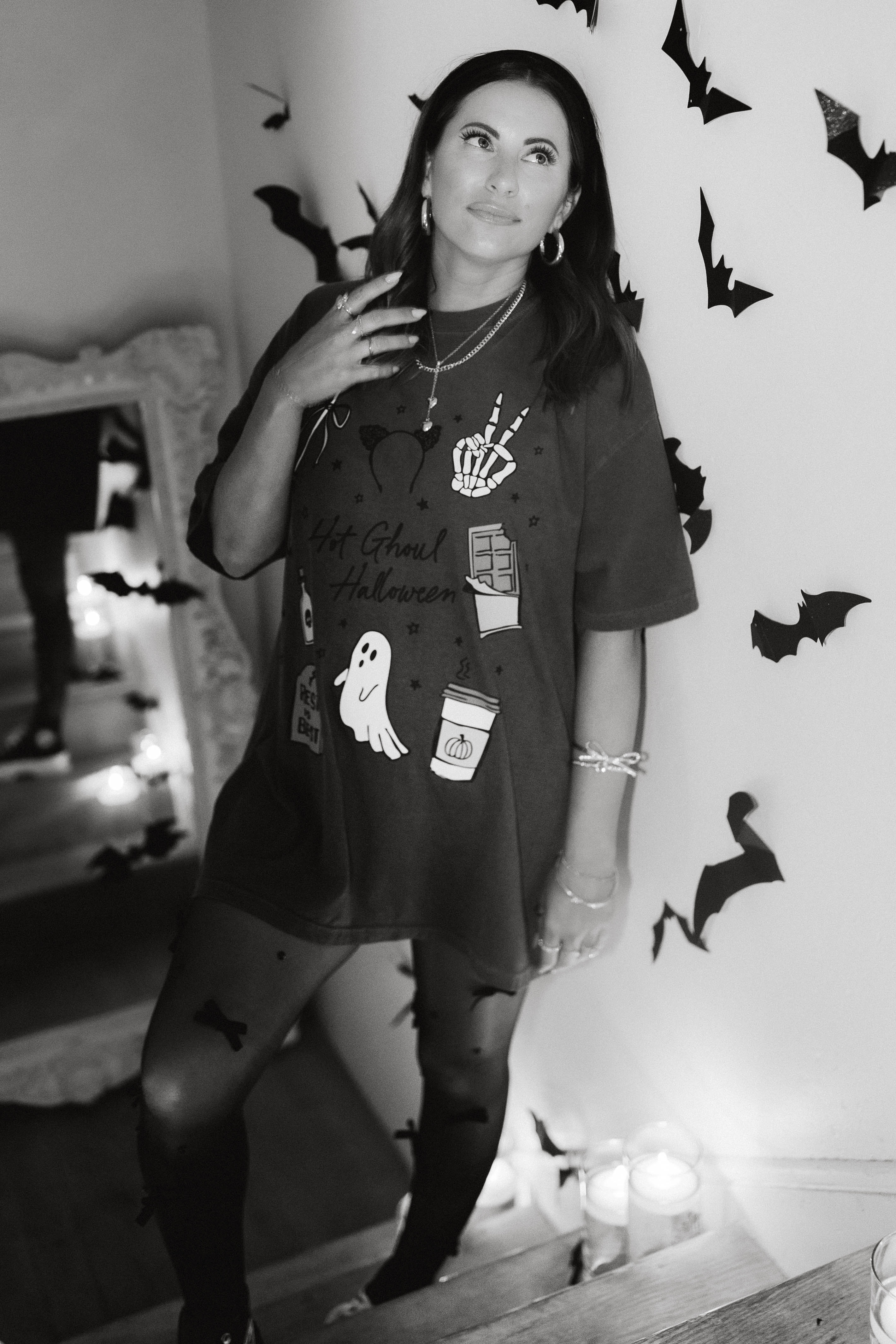 model krista in the staircase wearing hot ghoul halloween tee with halloween graphics and candles and bat decorations in the background - black and white photo