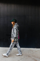 model walking away showing hot mess at heart camo hoodie and hot mess at heart hat against black wall 