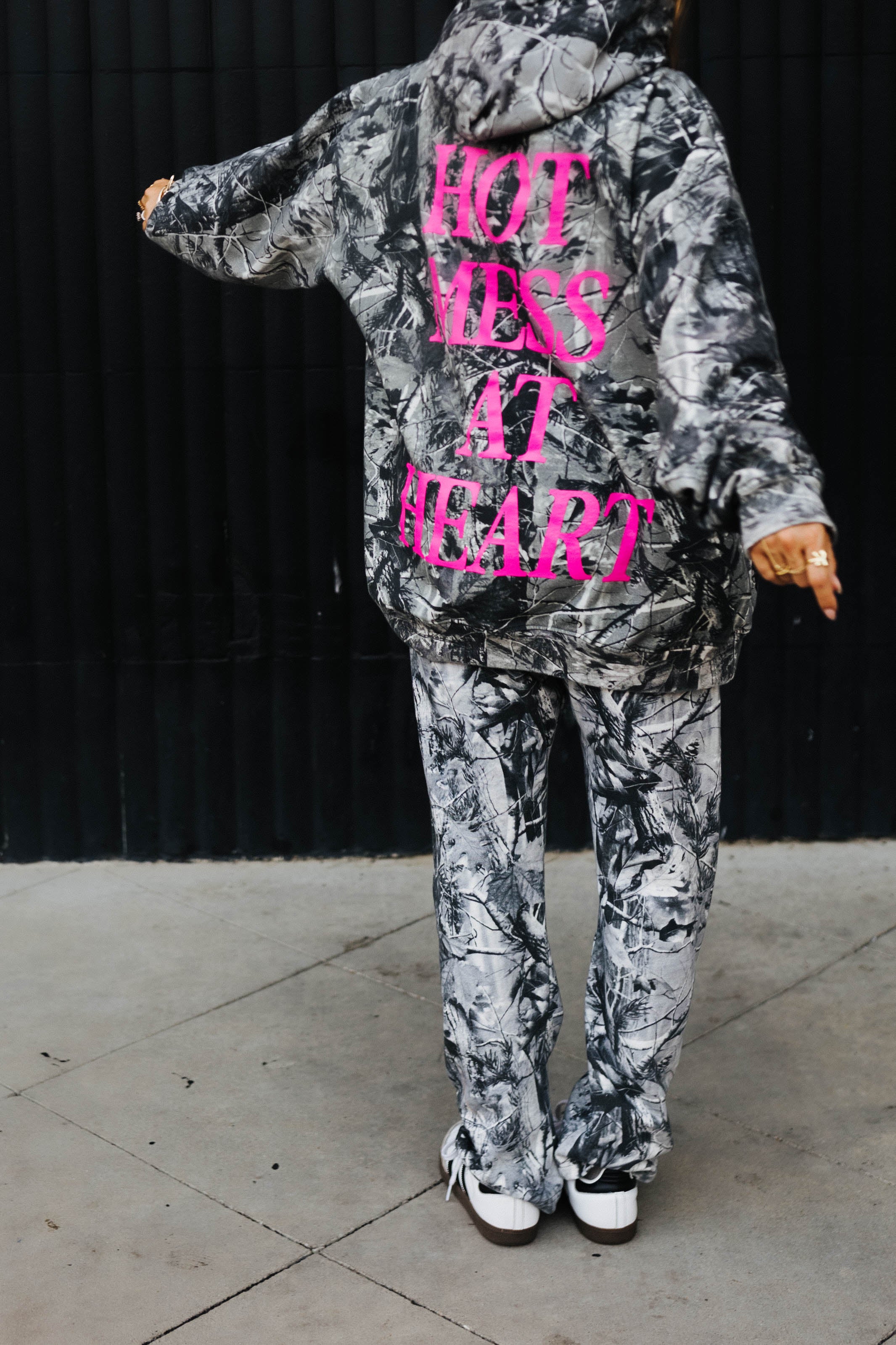 model swinging arms showing the back of the hot mess at heart camo hoodie with pink hot mess at heart text on the back 