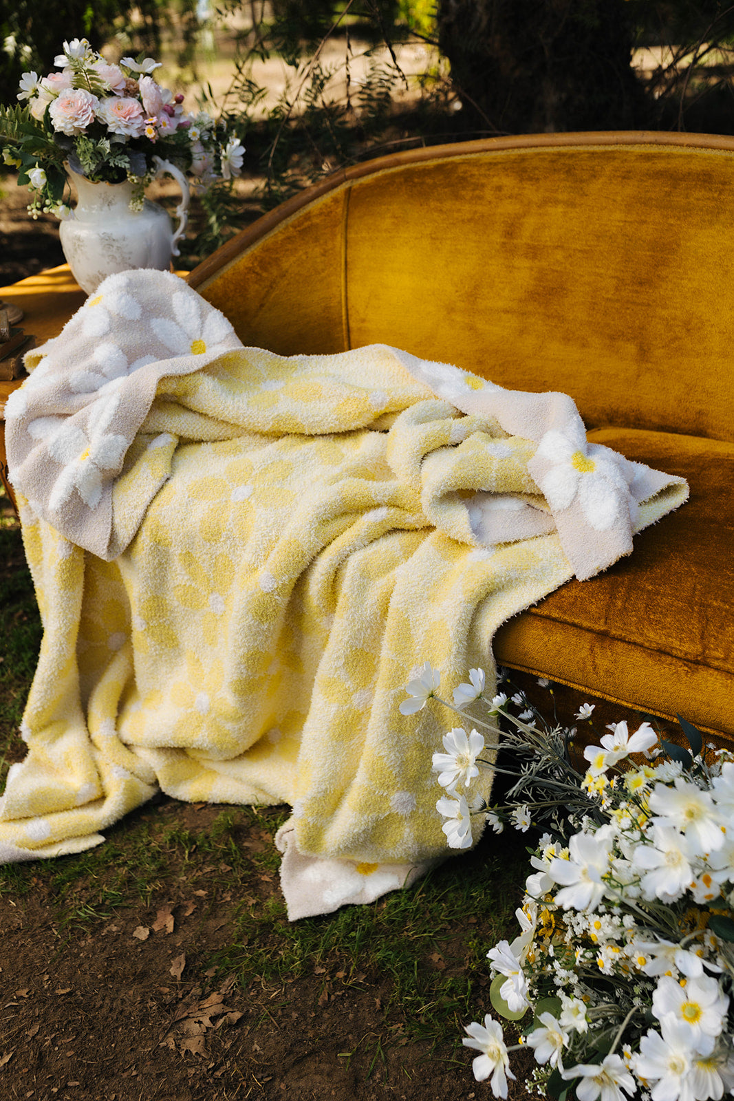 Yellow floral blanket draped over a mustard yellow couch with white flowers around.