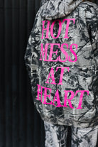 hot mess at heart pink text on back of camo hoodie with black wall in background