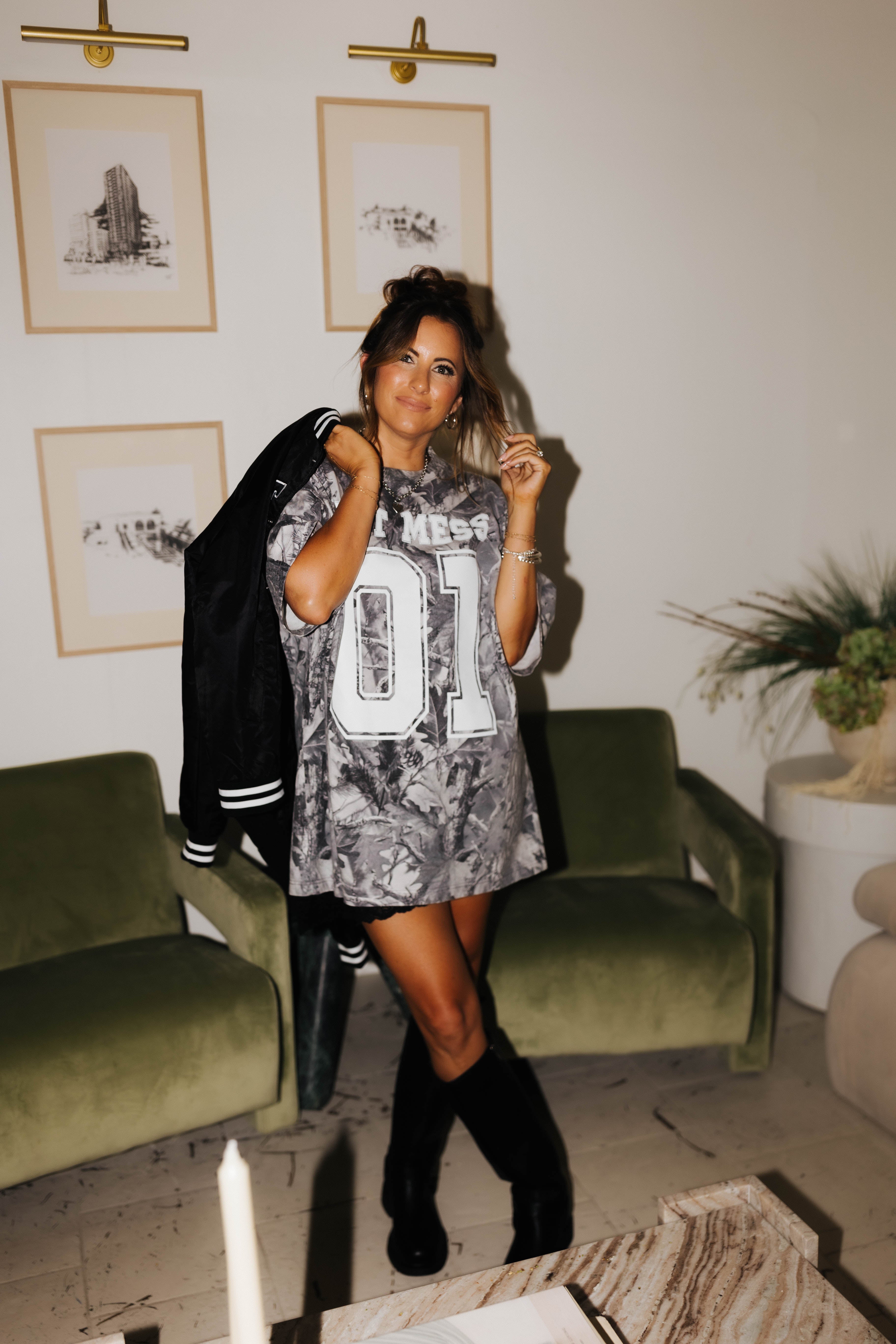 model krista smiling at camera wearing camo tee and hot mess bomber jacket over shoulder 