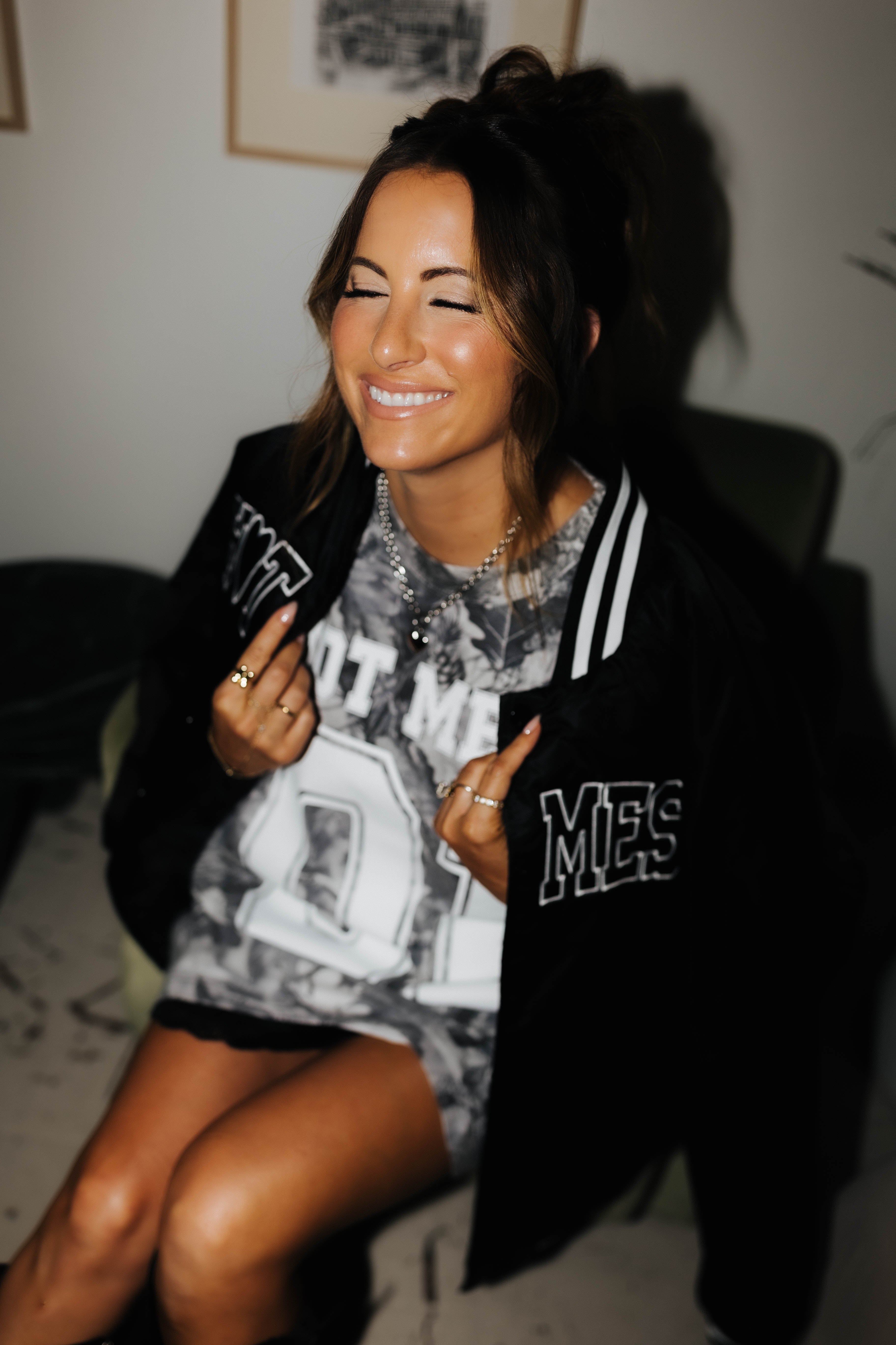 model smiling with eyes closed holding the hot mess bomber jacket over shoulders while wearing camo tee 