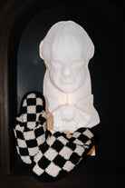 Sand and black check slippers displayed beside a decorative bust