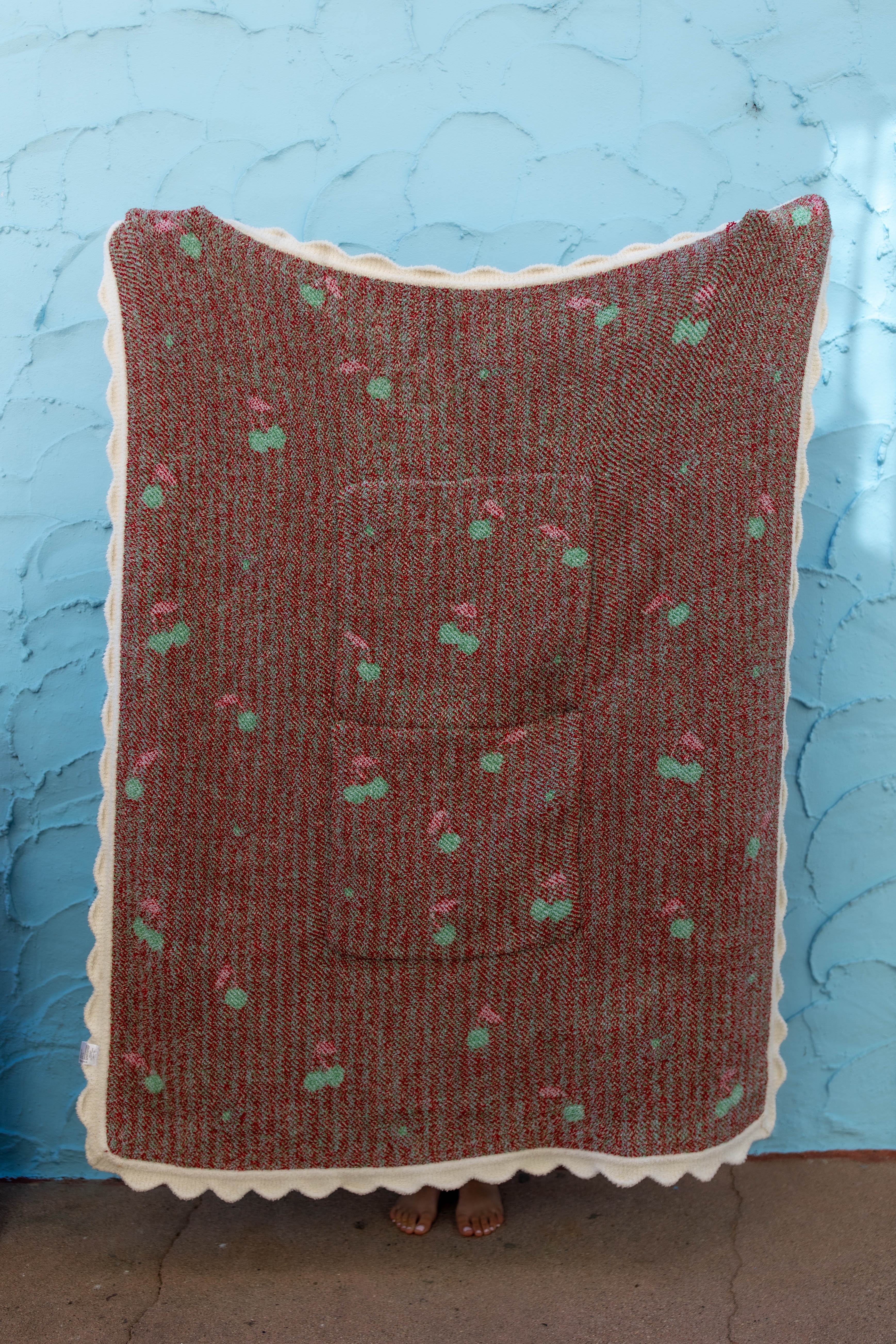 Back side of the cherry blanket showing the white scallop edge and mostly red background against a blue wall