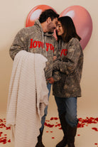 Two people in matching hoodies with heart balloons and red petals on the floor. Bryce holding the ribbed blanket