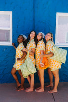 Four women posing together in matching orange printed pjs standing in front of a bright blue stucco wall.