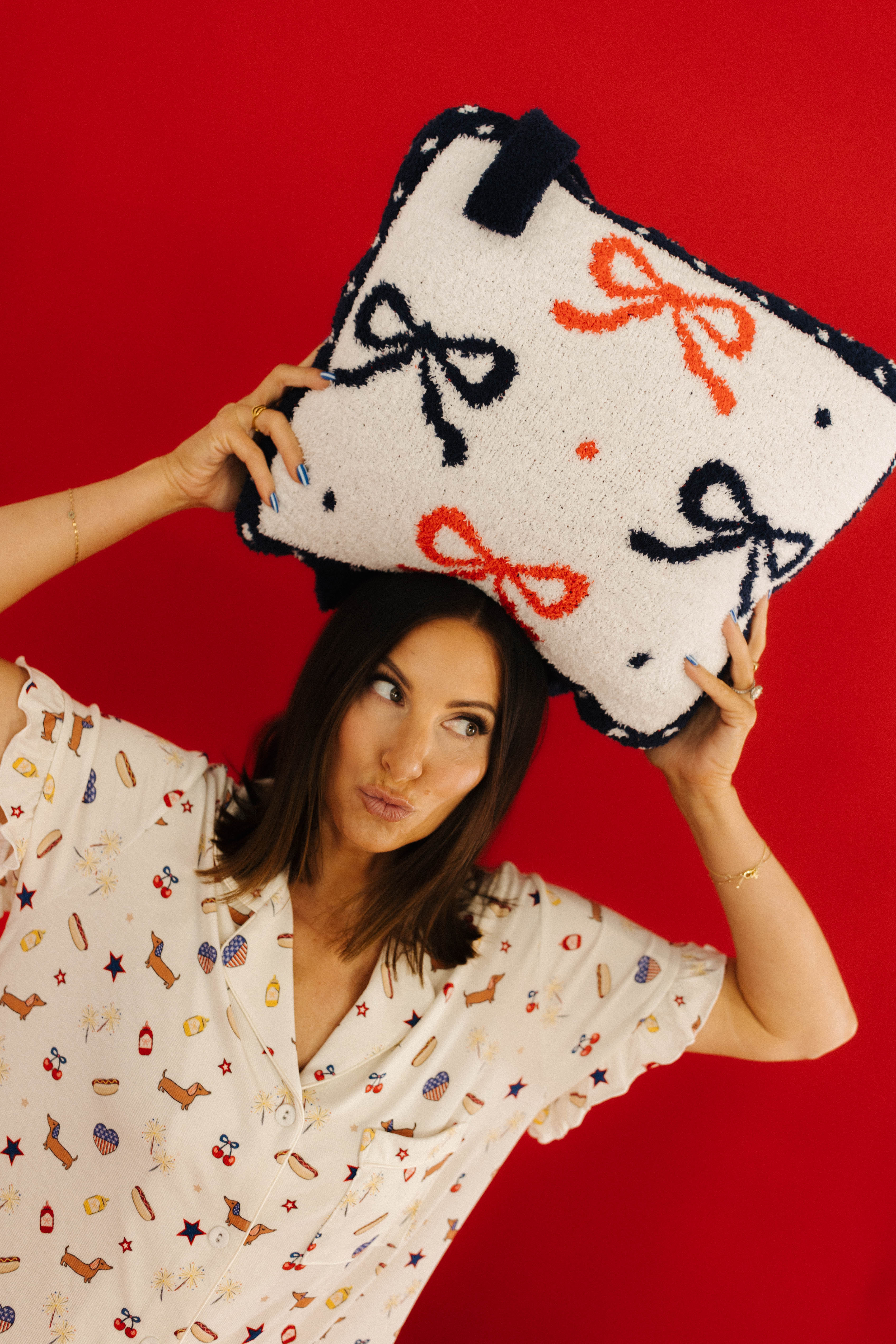 Woman holding a pillow on top of her head with bow designs against a red background