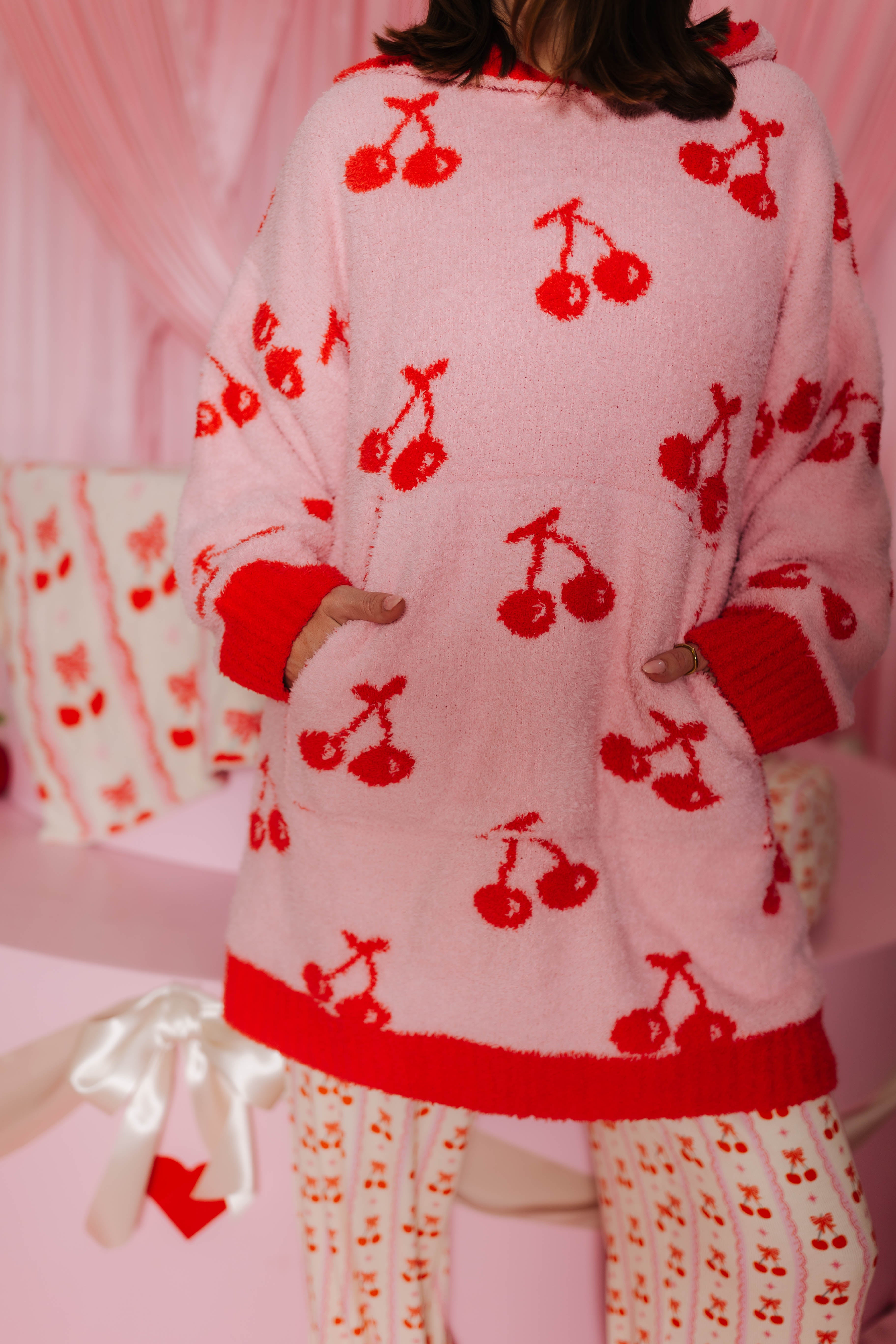 Person wearing a pink wearable with red cherry patterns in a pink room. Showing the pockets.