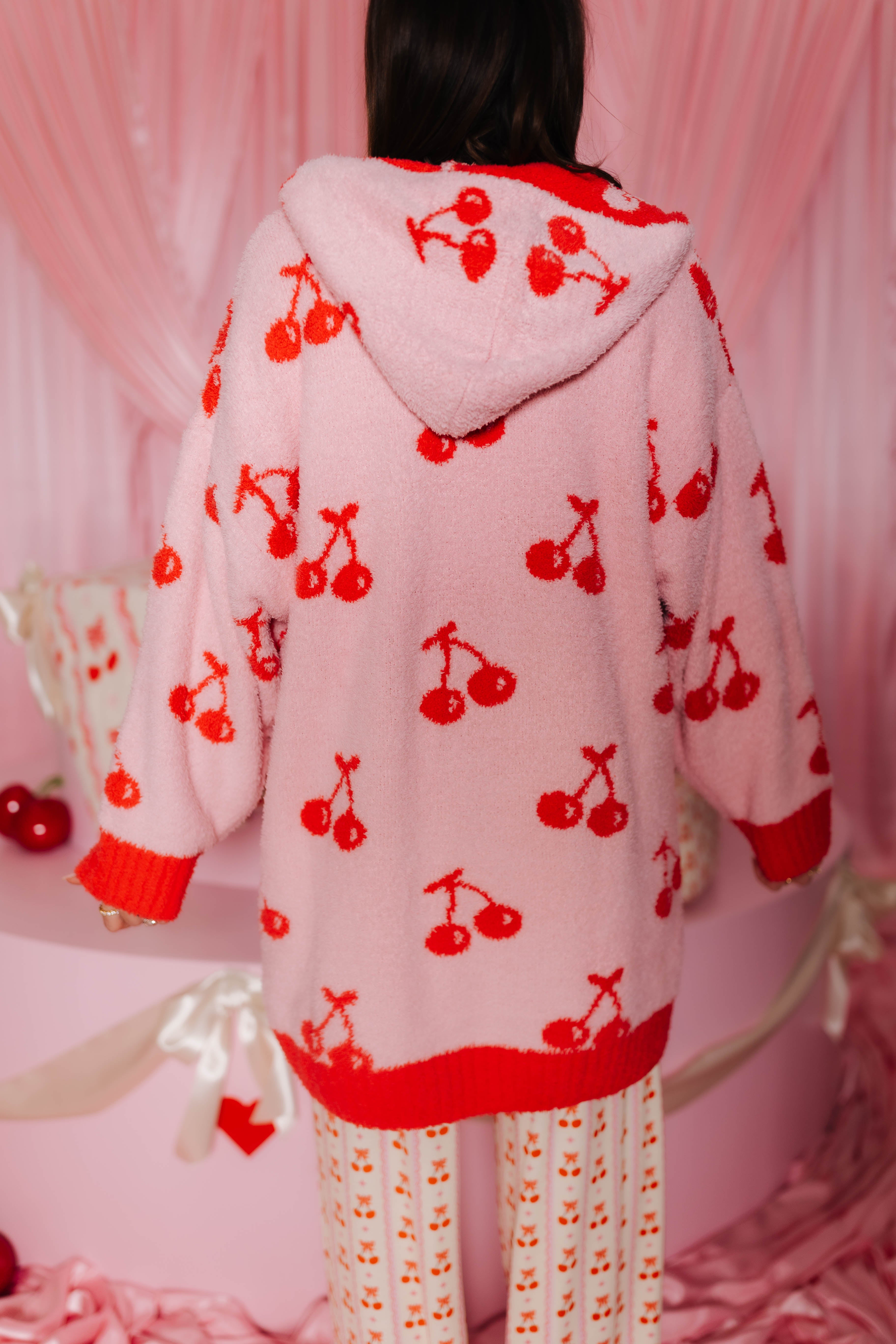 Person wearing a pink hoodie wearable with red cherry patterns in a pink-themed setting.