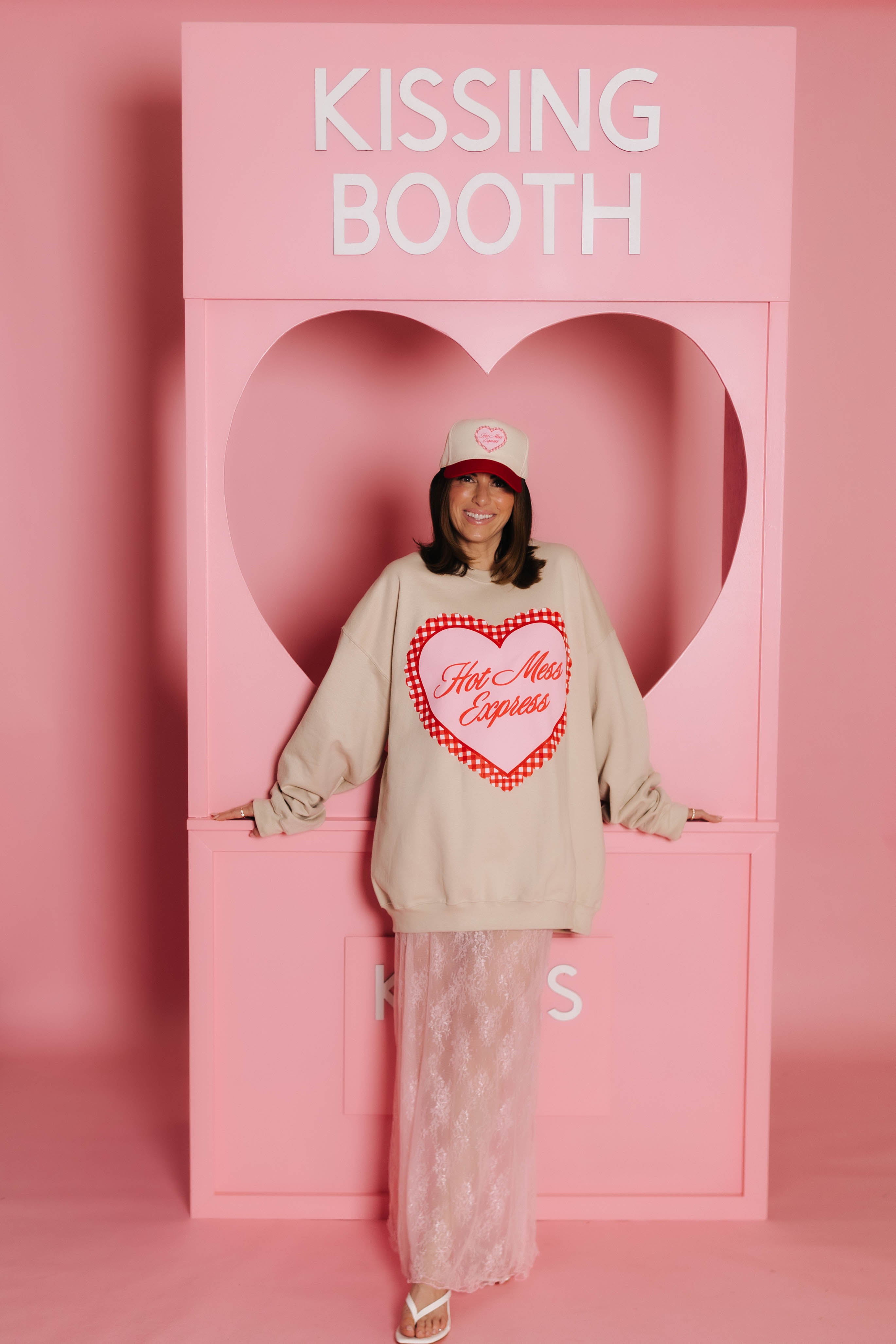 Krista standing in front of the kissing booth modeling the hot mess express sweatshirt.