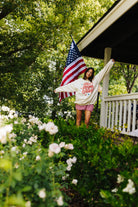 Woman standing in front of American flag on a porch with greenery and flowers