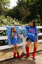 Two girls in blue shirts and red boots standing next to a white fence
