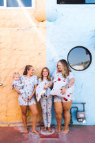 Four girls wearing matching strawberry-themed pajamas stand barefoot outdoors against a split yellow and light blue stucco wall all in matching cherry pajamas!
