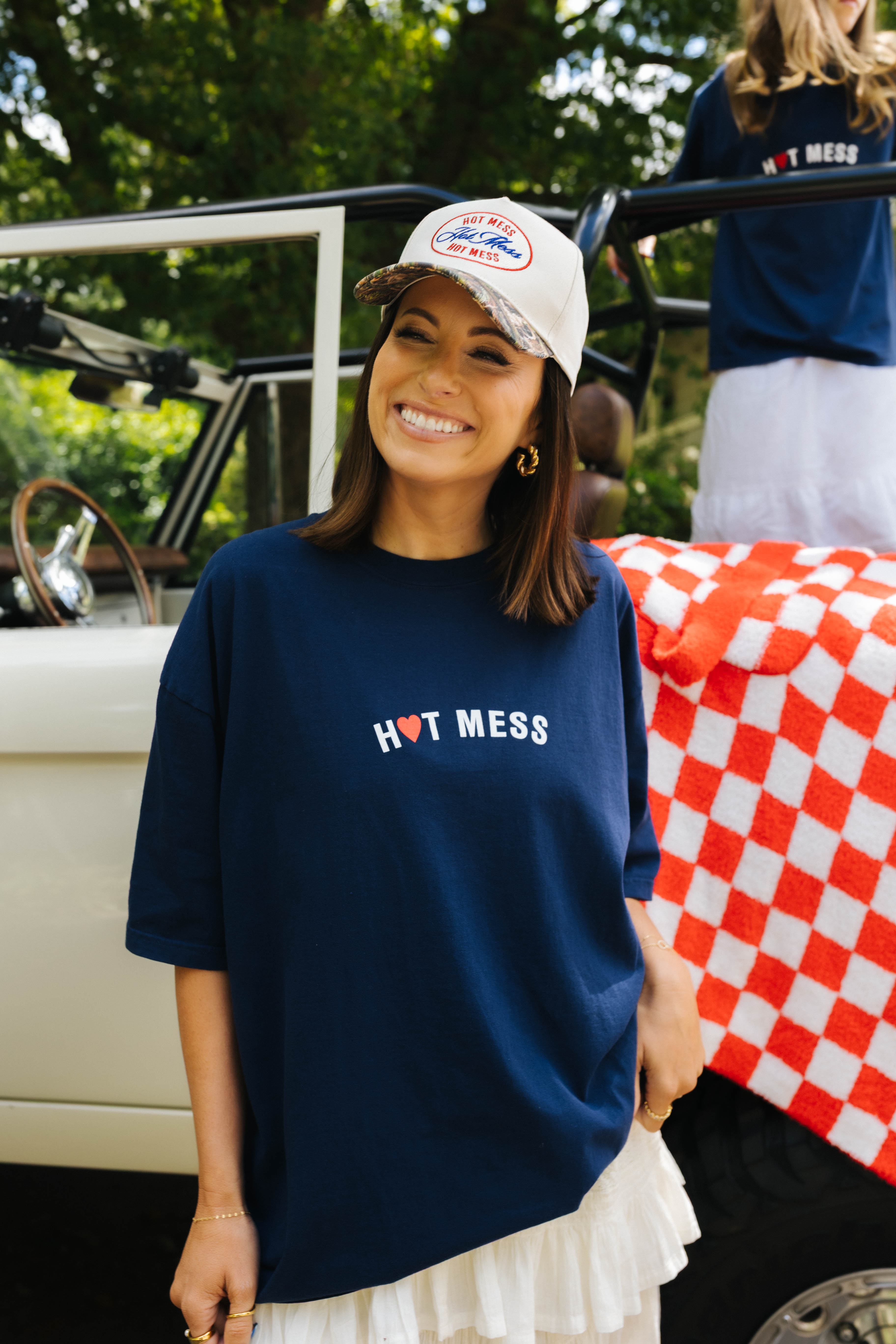 Woman wearing a navy 'HOT MESSES' t-shirt and white hat
