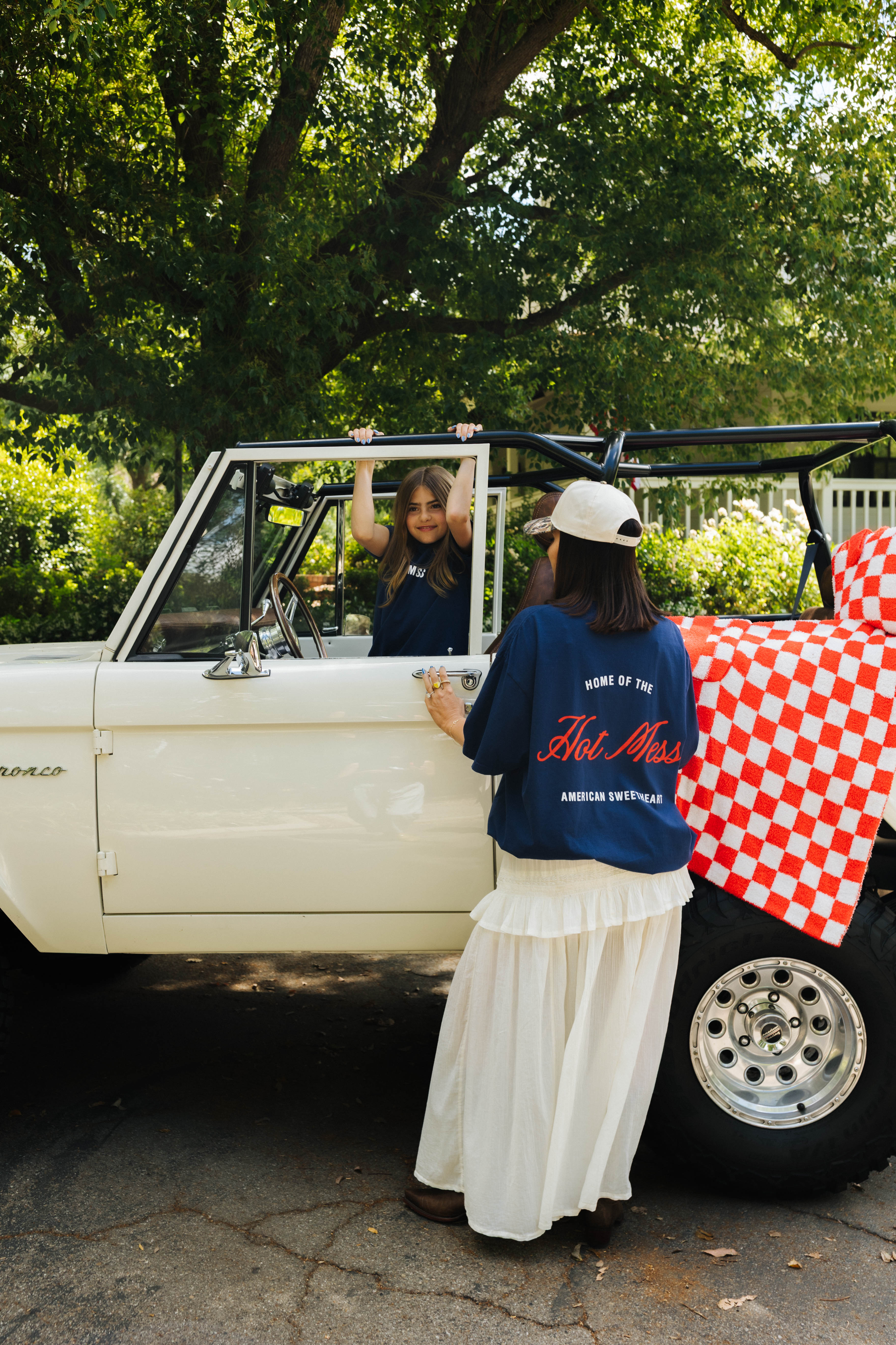Woman standing in front of a vintage bronco with home of the hot mess tee