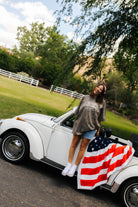 another photo of krista smiling on the bug with the american flag blanket styled on it 