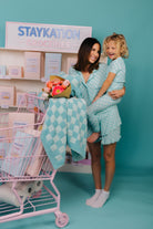Woman and child in matching teal outfits with a pink shopping cart and 'Staykation' sign.